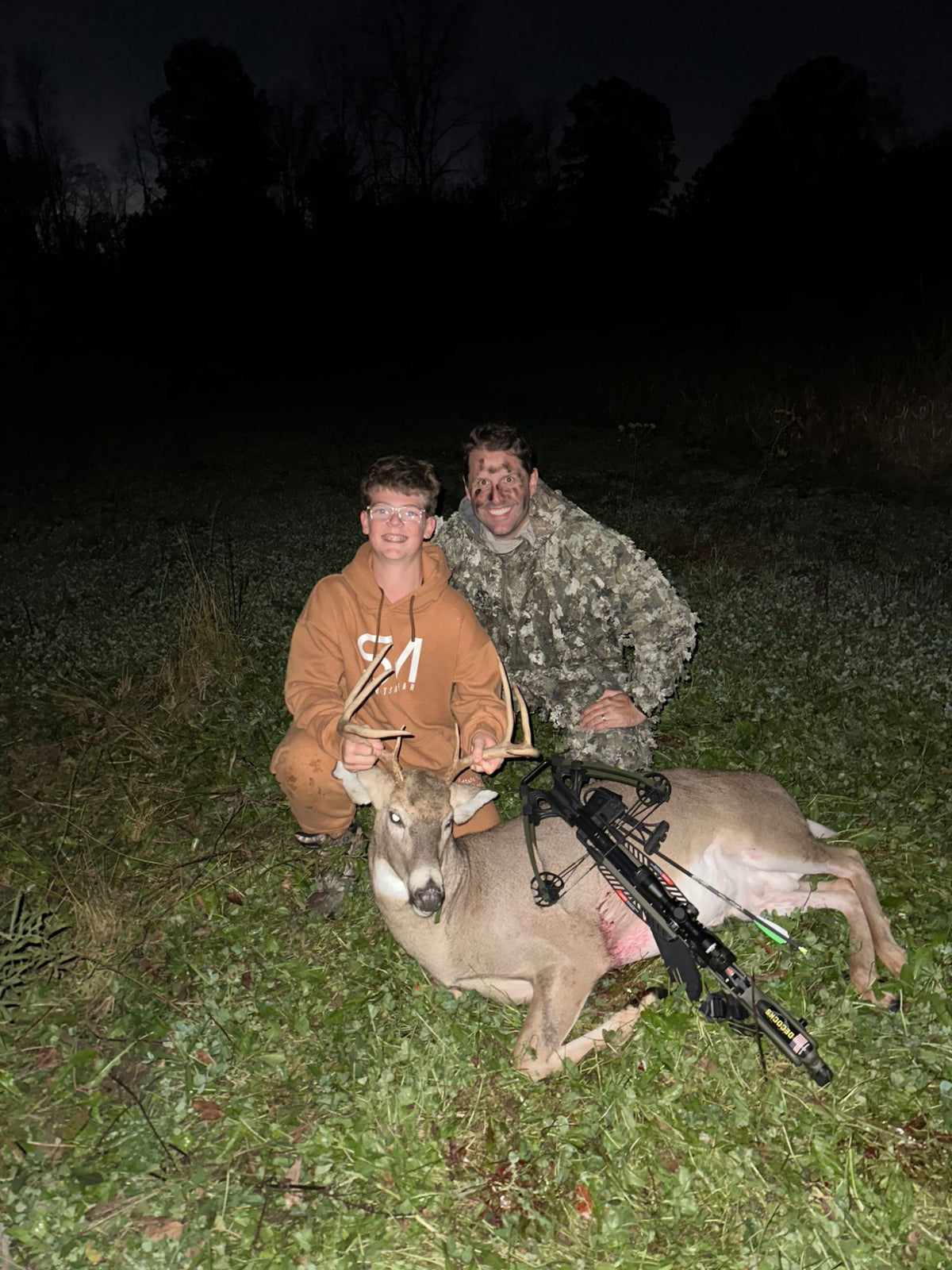 A young hunter and a man with a harvested buck and a crossbow