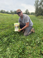 Plot Twist owner Matt kneeling in a clover plot with a bag of Multi-Season Clover Blend